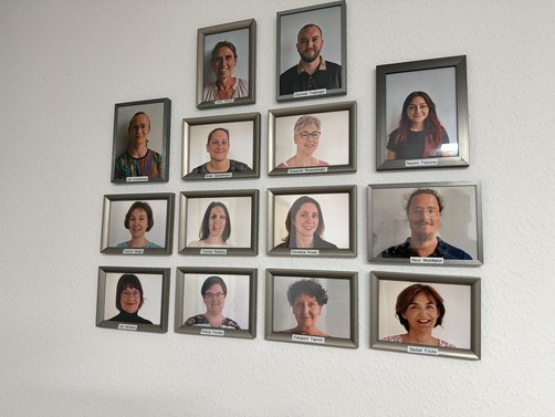 Fotowand mit gerahmten Porträtfotos des gesamten Praxisteams, jeweils mit Namensschild.